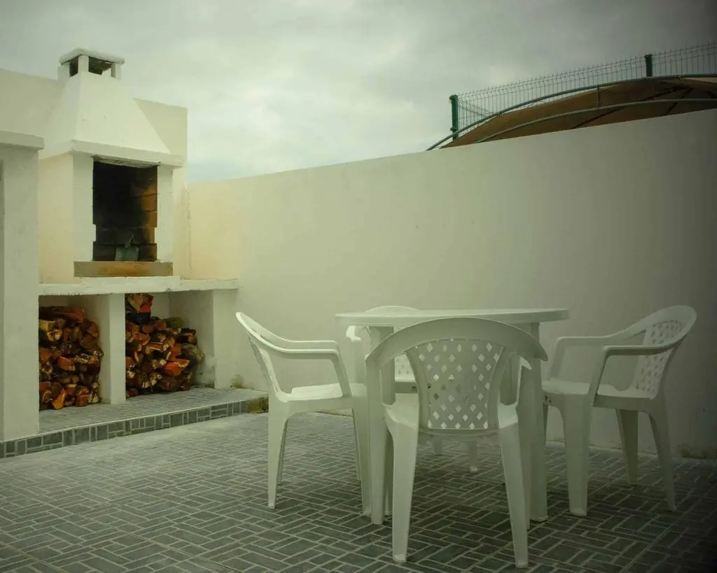 White outdoor dining set and traditional brick barbecue in a private guest house patio