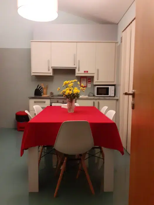 Dining area and kitchenette at Ponta Delgada Apartment T3 featuring a table with a red tablecloth, white chairs, yellow flowers, and white kitchen cabinets with a microwave