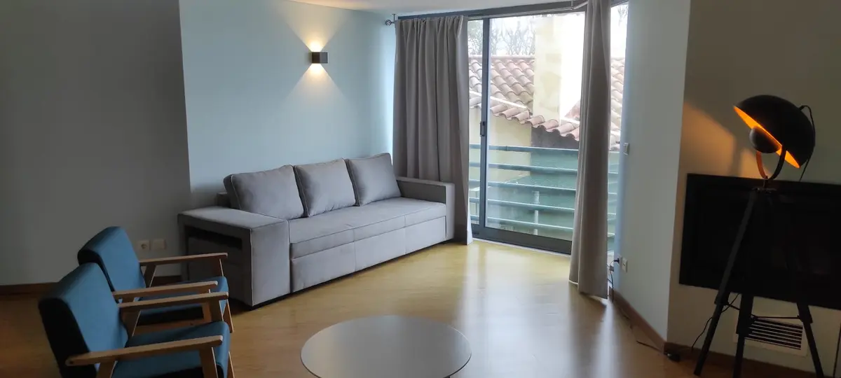 Modern living room at Ponta Delgada Apartment T3 featuring a grey sofa bed, two blue armchairs, a stylish floor lamp, and a large window with balcony access