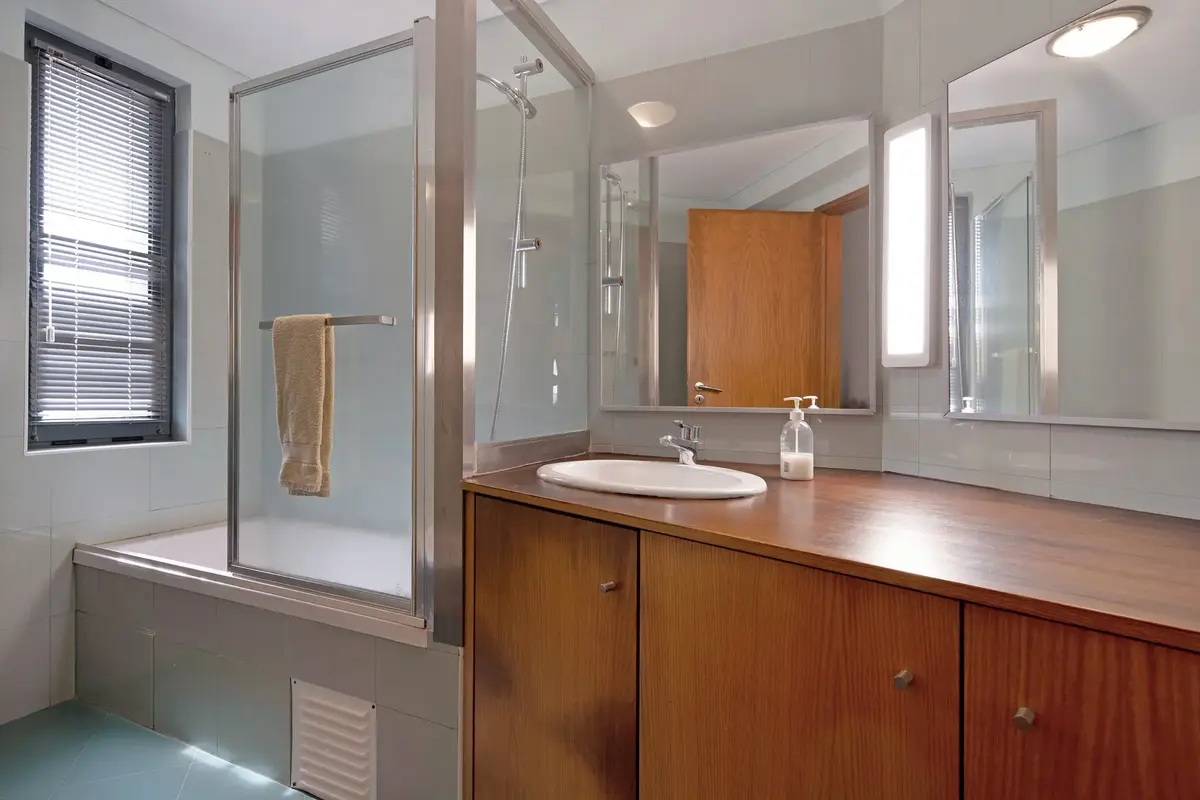 F Modern bathroom at Ponta Delgada Apartment T3 featuring a bathtub with a glass shower screen, a large wooden vanity with a white sink, and two large mirrors