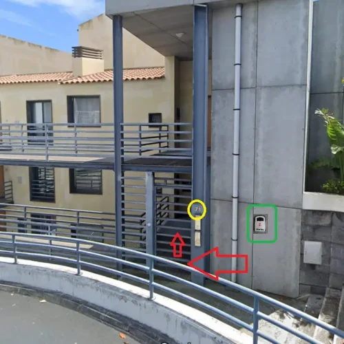 EN: Main entrance of the apartment complex for Ponta Delgada Apartment T3, featuring a secure metal gate with intercom, concrete walls, and outdoor access stairs. PT: Entrada principal do complexo de apartamentos do Ponta Delgada Apartment T3, apresentando um portão metálico de segurança com intercomunicador, paredes de betão e escadas de acesso exterior.