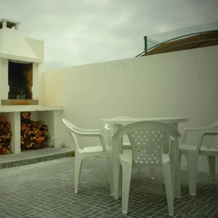 White outdoor dining set and traditional brick barbecue in a private guest house patio.