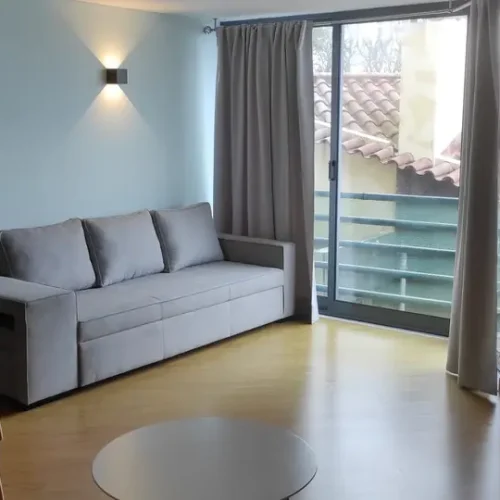 EN: Modern living room at Ponta Delgada Apartment T3 featuring a grey sofa bed, two blue armchairs, a stylish floor lamp, and a large window with balcony access. PT: Sala de estar moderna no Ponta Delgada Apartment T3 com sofá-cama cinzento, duas poltronas azuis, um candeeiro de pé elegante e uma janela grande com acesso à varanda.