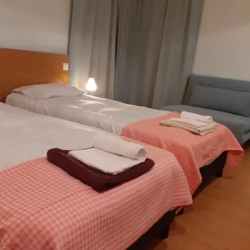 Twin bedroom configuration at Ponta Delgada Apartment T3 featuring two separate sommier beds with checkered linens, white towels, and a modern wooden headboard with integrated lighting. PT: Configuração de quarto twin no Ponta Delgada Apartment T3 com duas camas sommier separadas com roupa de cama axadrezada, toalhas brancas e cabeceira de madeira moderna com iluminação integrada.