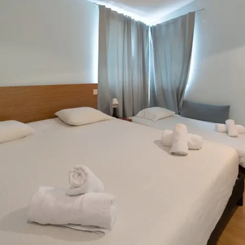 Versatile second bedroom at Ponta Delgada Apartment T3 featuring two twin beds joined as a double, an additional prepared sofa bed, white linens, and wooden headboard. PT: Segundo quarto versátil no Ponta Delgada Apartment T3 com duas camas twin juntas como casal, um sofá-cama adicional preparado, roupa de cama branca e cabeceira em madeira.